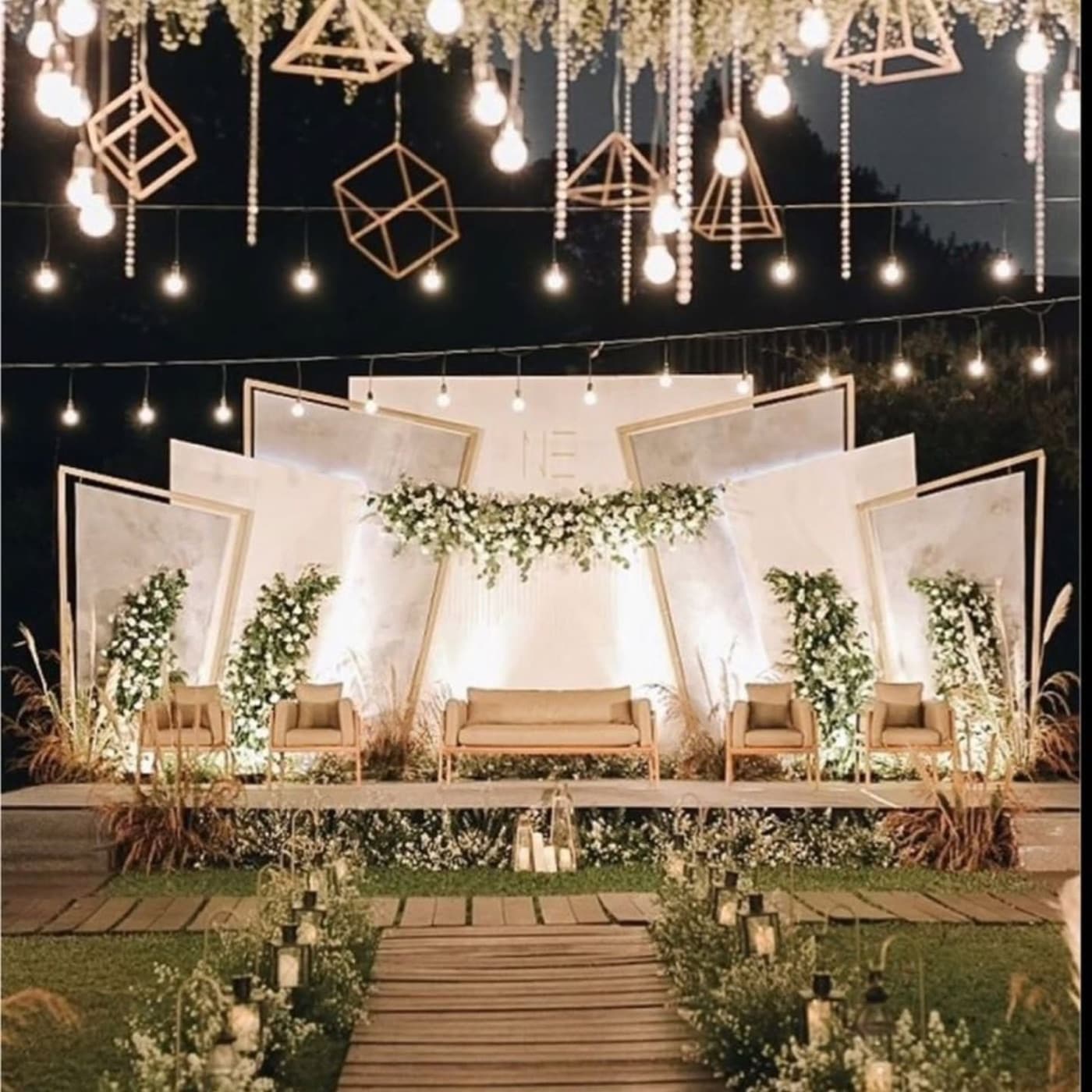 An evening stage set with warm string lights, geometric hanging frames and greenery