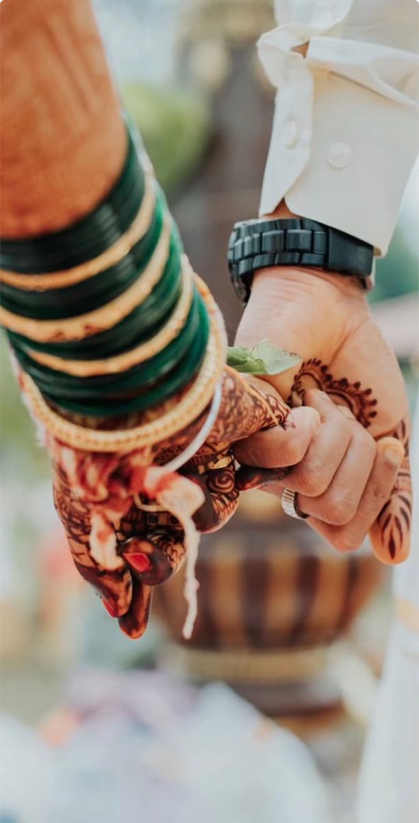 Bangled and mehendi-covered hands held by a groom's hand