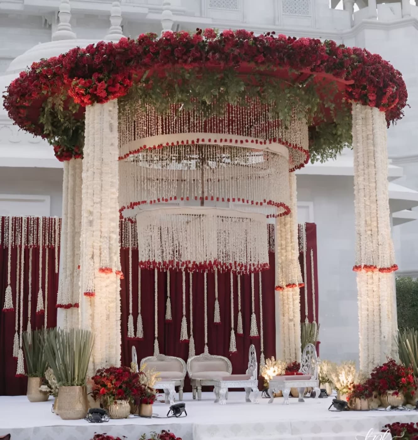 A crimson and ivory mandap with hanging floral strands and carved pillars